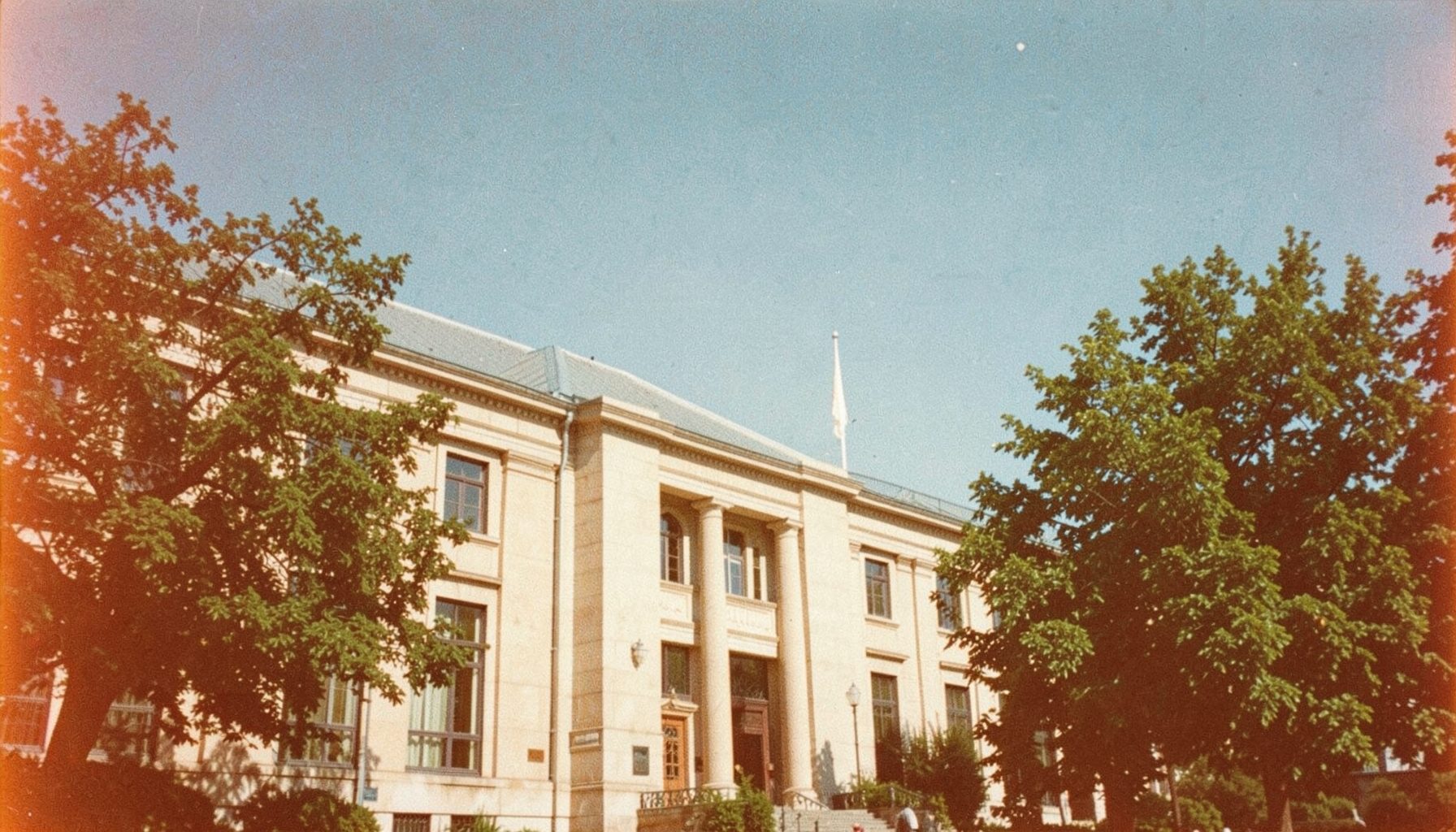 Government building exterior with trees and a clear blue sky, formal institutional architecture in beige stone